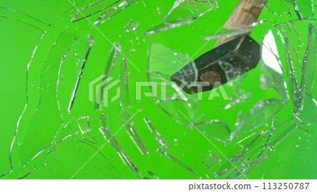 Freeze motion of glass-breaking hammer, shattering against green background 113250787