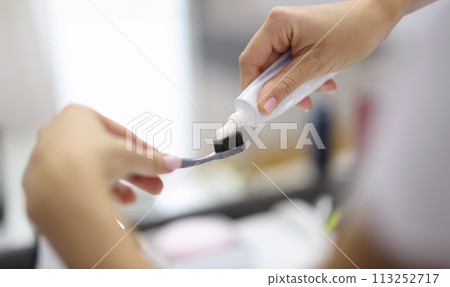 Female hand squeezing toothpaste from tube onto toothbrush close-up Female hand squeezing toothpaste from tube onto toothbrush close-up 113252717