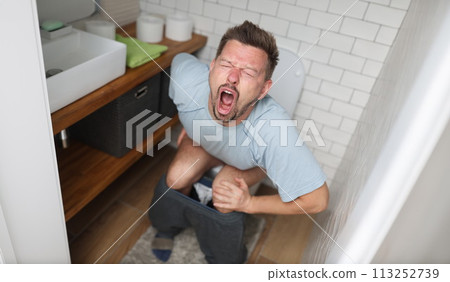 Young man with suffering on his face sits on toilet in bathroom 113252739