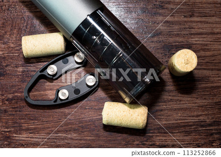 An electric corkscrew and wine bottle caps lie on a dark wood table, preparing for the holiday An electric corkscrew and wine bottle caps lie on a dark wood table, preparing for the holiday 113252866