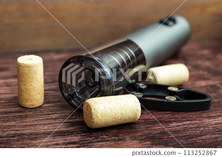 An electric corkscrew and wine bottle caps lie on a dark wood table, preparing for the holiday An electric corkscrew and wine bottle caps lie on a dark wood table, preparing for the holiday 113252867