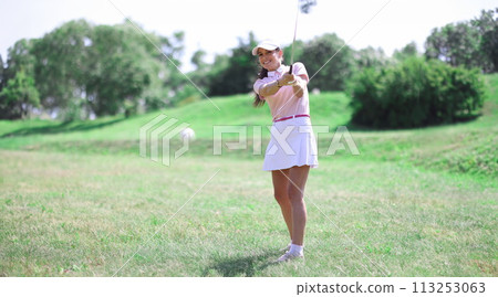Beautiful woman in white skirt, cap and pink t-shirt play golf on green lawn. 113253063