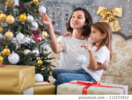 Mom and daughter holding Christmas decorations on Christmas tree 113253952