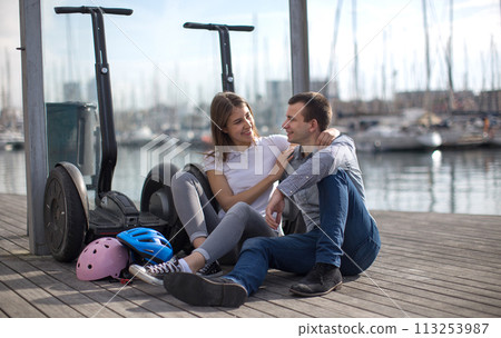Young couple guy and girl are walking on the segway along the board paved promenade in the port of a European city 113253987