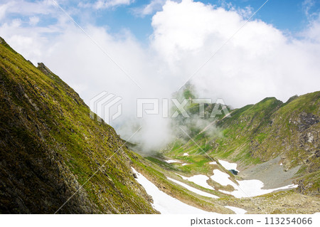 alpine landscape in summer. spots of snow among grass on the rocky hills of fagaras range beneath a sky with clouds. popular travel destination in the mountains of romania 113254066