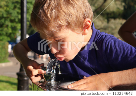 Boy drinks water from street tap on hot summer day. To quench his thirst. Close-up 113254642