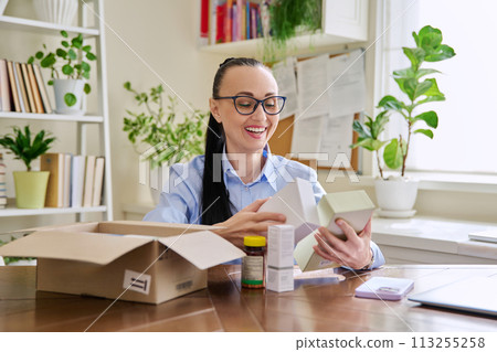 Female customer sitting at home unpacking cardboard box with online purchases 113255258