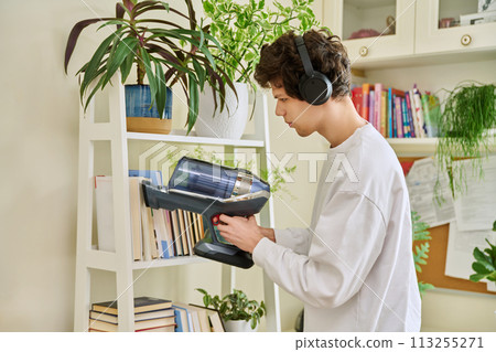 Young man wearing headphones vacuums bookshelves at home Young man wearing headphones vacuums bookshelves at home 113255271