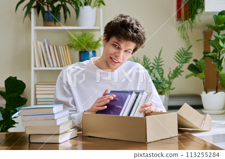Satisfied young male customer unpacking cardboard box with online purchases, new books 113255284