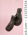 a pair of old boxing gloves hung in front of a candy-pink background 113255434