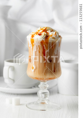 Iced caramel latte topped with whipped cream and caramel sauce. 113255681