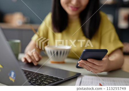 Selective focus shot of young Asian woman reading message on smartphone while scrolling web page in Internet on smartphone during breakfast Selective focus shot of young Asian woman reading message on smartphone while scrolling web page in Internet on smartphone during breakfast 113255749