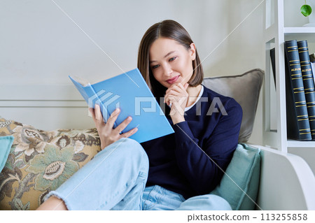 Young woman reading book, relaxed sitting on couch at home Young woman reading book, relaxed sitting on couch at home 113255858