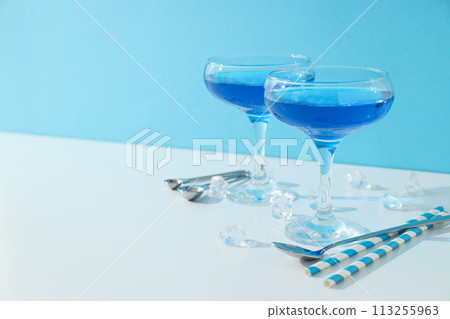 Blue cocktail in glass, spoons, straws and ice cubes on blue background, space for text Blue cocktail in glass, spoons, straws and ice cubes on blue background, space for text 113255963
