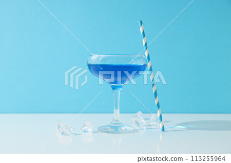 Blue cocktail in glass, straw and ice cubes on blue background Blue cocktail in glass, straw and ice cubes on blue background 113255964