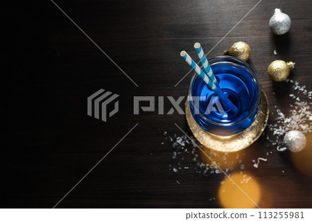 Blue cocktail with straws in glass, snow and balls on wooden background, space for text Blue cocktail with straws in glass, snow and balls on wooden background, space for text 113255981