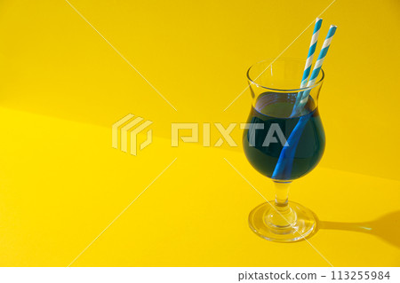 Blue cocktail with straws in glass on yellow background, space for text Blue cocktail with straws in glass on yellow background, space for text 113255984