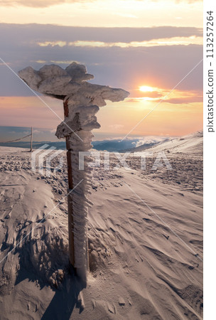 Snow covered pointer near path on snowy mountain plateau and sunshine in sky. Magnificent sunny day on picturesque beautiful alps ridge. 113257264