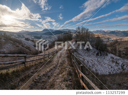 Winter coming. Last good weather days in autumn mountain countryside morning picturesque scene. Dirty road from hills to the village. Hoverla and Petros Ukrainian Carpathians mountains in far. 113257299