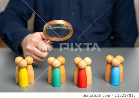 The concept of market segmentation. Target audience, customer care. Market group of buyers. Customer relationship management. Businessman looking through a magnifying glass at figurines of people 113257815