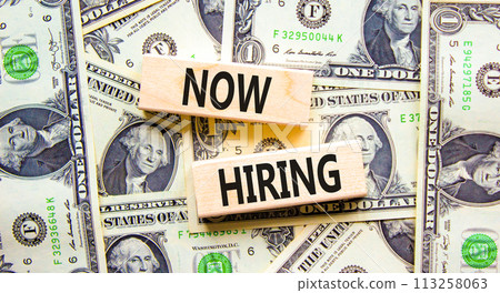 Now hiring symbol. Concept words Now hiring on beautiful wooden block. Beautiful background from dollar bills. Dollar bills. Business marketing, motivational now hiring concept. Copy space. 113258063