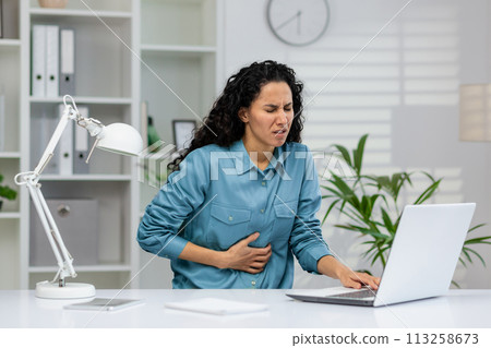 Professional woman experiencing discomfort while seated at a workstation, indicating possible health issues at work. 113258673
