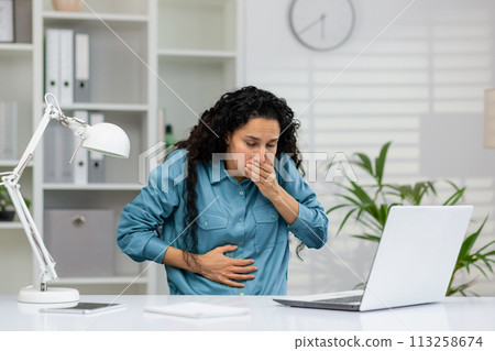 An adult woman experiencing nausea at her desk with a hand over her mouth and holding her stomach, possibly indicating sickness or discomfort. 113258674