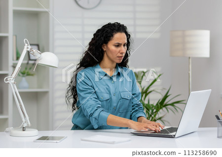 Professional female executive engaged in concentration while using laptop at a well-organized workplace with indoor plants. Professional female executive engaged in concentration while using laptop at a well-organized workplace with indoor plants. 113258690