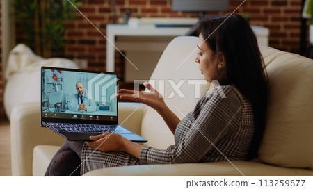Patient sitting on couch, receiving treatment plan from medic during online videocall meeting after medical checkup. Indian person receiving prescription from GP in telemedicine call, camera B Patient sitting on couch, receiving treatment plan from medic during online videocall meeting after medical checkup. Indian person receiving prescription from GP in telemedicine call, camera B 113259877