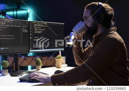Cybersecurity specialist drinking coffee while looking for company security vulnerabilities and preventing malware infections. Programmer enjoying hot beverage while installing fortified code on PC Cybersecurity specialist drinking coffee while looking for company security vulnerabilities and preventing malware infections. Programmer enjoying hot beverage while installing fortified code on PC 113259965