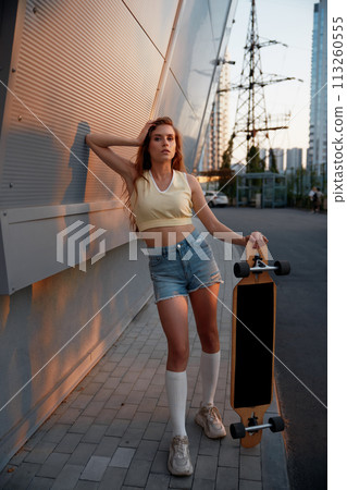 Young woman with longboard standing over cityscape background 113260555