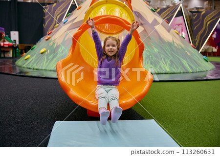 Cute little girl child riding on slide at indoor playground Cute little girl child riding on slide at indoor playground 113260631