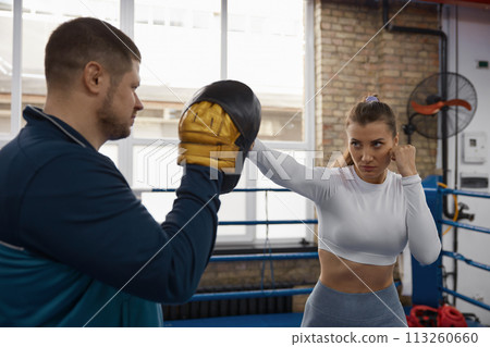 Athletic woman punching to man trainer on taebo training lesson at gym Athletic woman punching to man trainer on taebo training lesson at gym 113260660