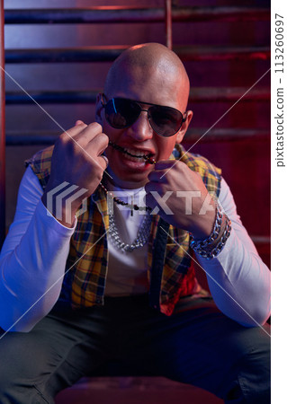 Portrait of young handsome hipster man with bald head biting beads Portrait of young handsome hipster man with bald head biting beads 113260697