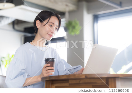 A beautiful smiling Asian (Japanese) woman drinking coffee and working on a computer in a beautiful office or cafe 113260908