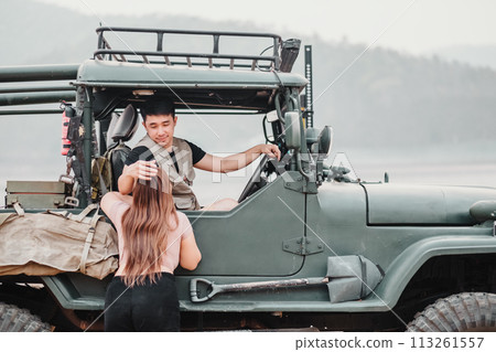 Caring man assists a woman as she climbs into a sturdy off-road car for an adventure by a misty lake at dawn. Caring man assists a woman as she climbs into a sturdy off-road car for an adventure by a misty lake at dawn. 113261557