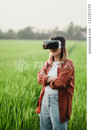 Confident young woman stands with arms crossed in a lush green field, wearing a VR headset, ready to explore virtual landscapes. Confident young woman stands with arms crossed in a lush green field, wearing a VR headset, ready to explore virtual landscapes. 113261570