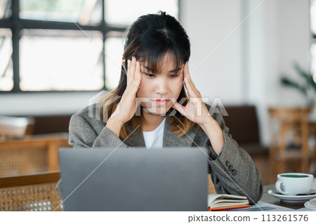 Businesswoman feeling overwhelmed with stress at work, holding head in hands in front of laptop at a cafe. Businesswoman feeling overwhelmed with stress at work, holding head in hands in front of laptop at a cafe. 113261576