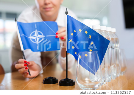 Young woman puts NATO and EU flags on table in office 113262537