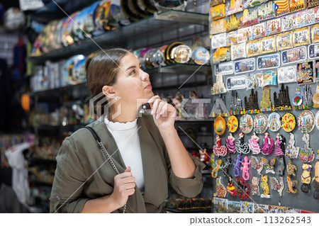 Happy female tourist looking to buy tourist magnets at gift shop 113262543