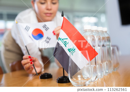 Unrecognizable girl sets midget flags of Iraq and South Korea before international negotiations 113262561