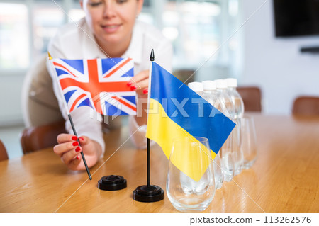 National flags of Ukraine and United Kingdom in female hands on negotiating table 113262576