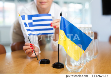 Female hands arranging flags of Greece and Ukraine on table before international meeting Female hands arranging flags of Greece and Ukraine on table before international meeting 113262614