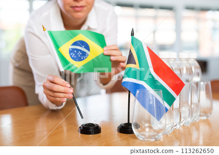 Little flag of South Africa on table and flag of Brazil put next to it by young woman Little flag of South Africa on table and flag of Brazil put next to it by young woman 113262650