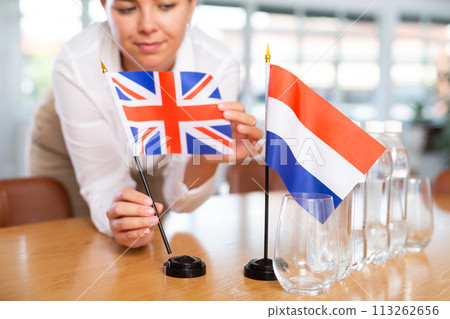 Young woman puts UK and Netherlands flags on table in office 113262656
