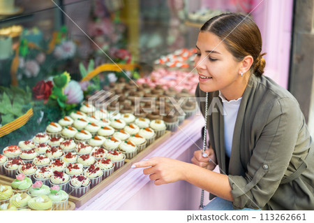Young woman chooses sweet cupcake at confectionery shop 113262661