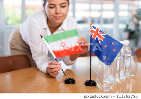 Young woman putting flags of Iran and New Zealand on table in office Young woman putting flags of Iran and New Zealand on table in office 113262750