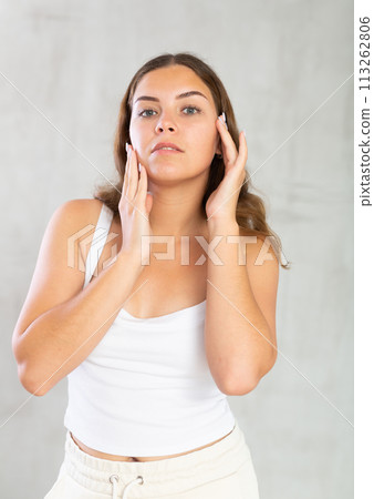 Young woman in casual clothes taking care of her skin Young woman in casual clothes taking care of her skin 113262806