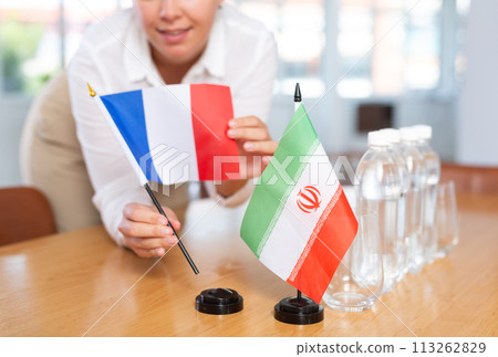 Woman secretary prepares the negotiating table - arranges flags of France and Iran Woman secretary prepares the negotiating table - arranges flags of France and Iran 113262829