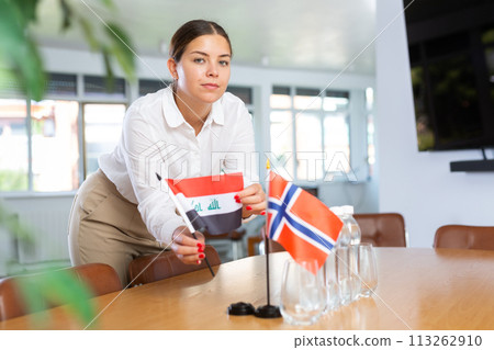 Positive young woman putting little flag of Iraq on table next to the flag of Norway Positive young woman putting little flag of Iraq on table next to the flag of Norway 113262910